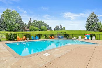 A large outdoor swimming pool surrounded by a black fence and lounge chairs.